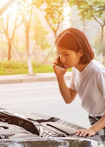 Young person on phone while looking at an issue under their car hood
