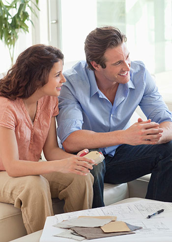 Man and woman sitting on a couch smiling while discussing home building plans