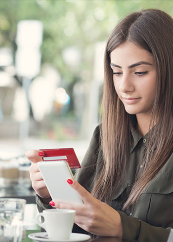 young woman holding her debit card while on her phone at a cafe