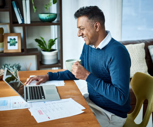 Man working on a laptop holding coffee mug