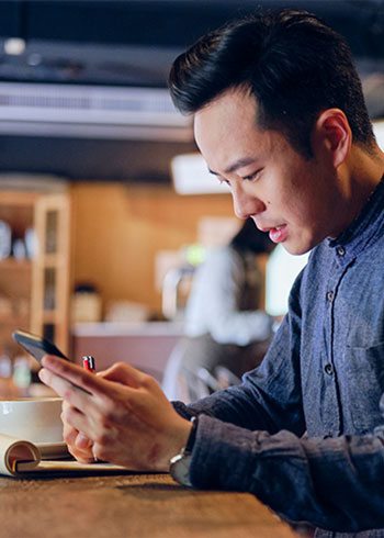 Man holding a pen to paper while looking at his phone