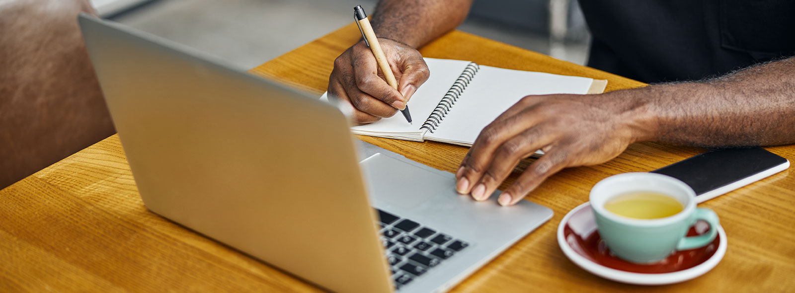 Man with pen to paper while looking at his laptop