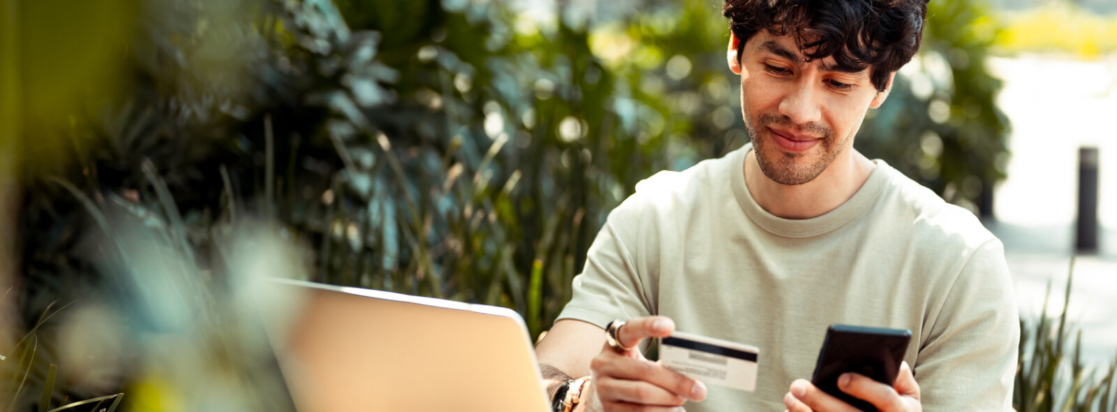 Young man holding mobile phone and credit/debit card outdoors