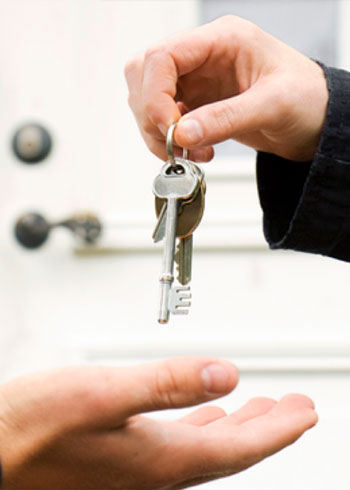 A person holding keys above someone else's open hand in front of a door to a home